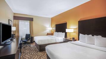 A hotel room with two beds, a desk with a flat-screen TV, a chair, and a desk lamp.