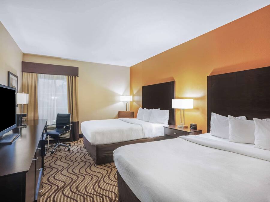 A hotel room with two beds, a desk with a flat-screen TV, a chair, and a desk lamp.