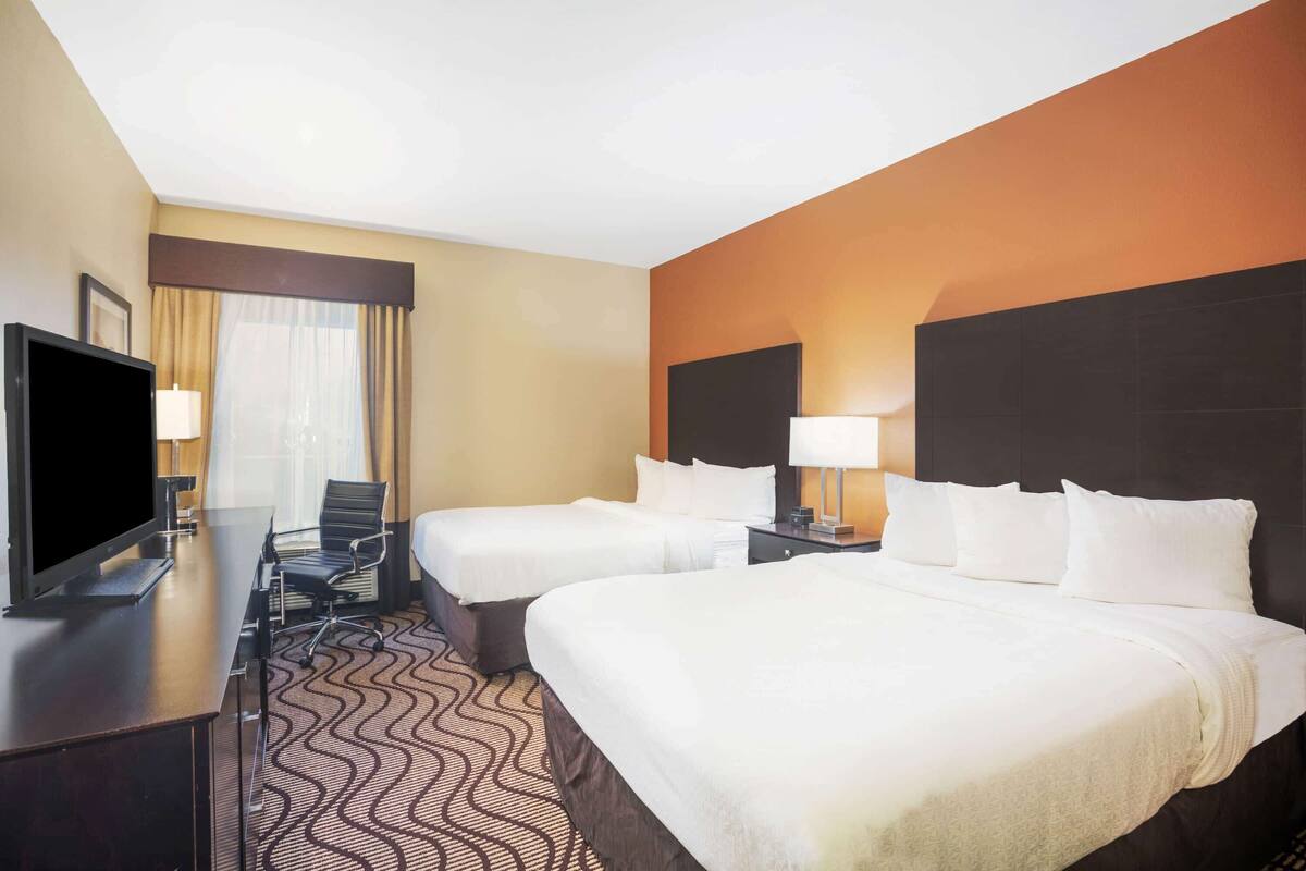 A hotel room with two beds, a desk with a flat-screen TV, and a chair.