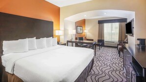 Ein Hotelzimmer mit einem großen Bett, einem Schreibtisch, zwei Stühlen, einem Fernseher und einem Fenster mit Vorhängen.