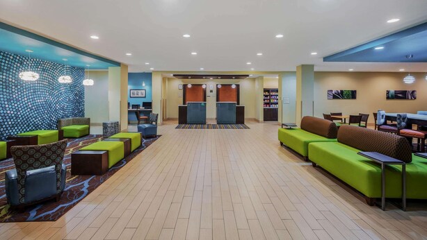 Eine großzügige Lobby mit grünen und braunen Sitzbereichen, einem Empfangstresen und einer Wand mit Musterdesign.