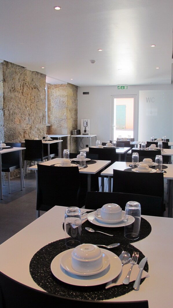 A dining area with tables set for service, a stone wall, and a WC sign. - V Dinastia (Lisbon)
