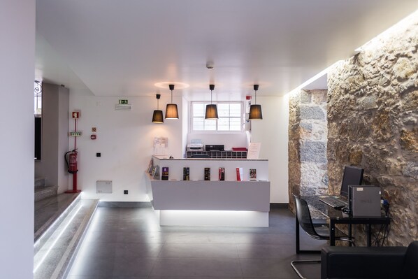 A reception area with a white counter, multiple pendant lights, a stone wall, and a desk with a computer. - V Dinastia (Lisbon)