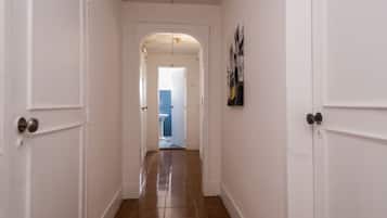 Un pasillo con paredes blancas y suelo de madera que conduce a un baño con inodoro azul.
