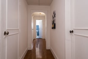 A hallway with white walls and wooden flooring, leading to a bathroom with a blue toilet. - V Dinastia (Lisbon)
