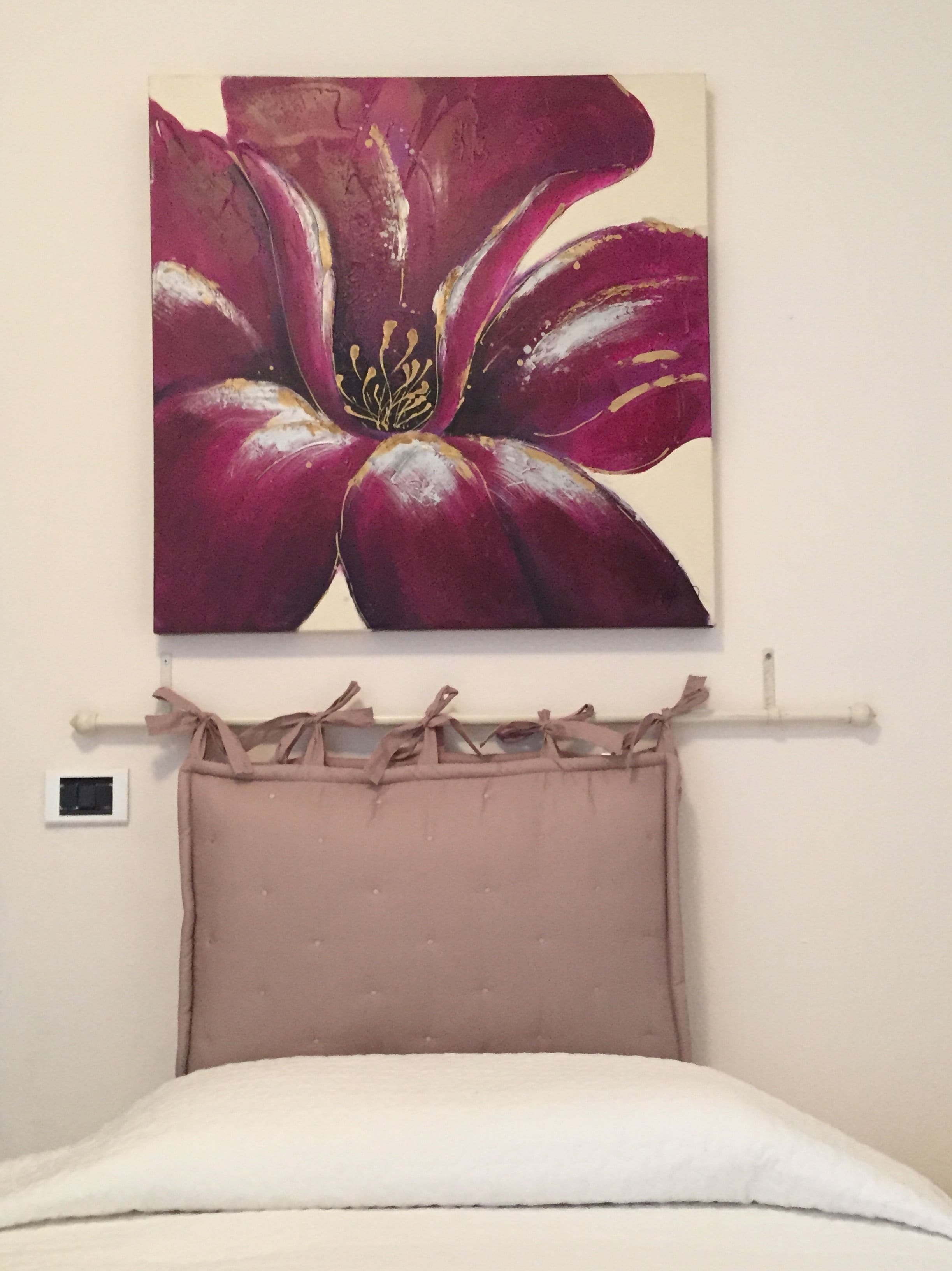 Une chambre à coucher avec un lit, un tableau représentant une fleur accroché au mur et un interrupteur sur le mur.