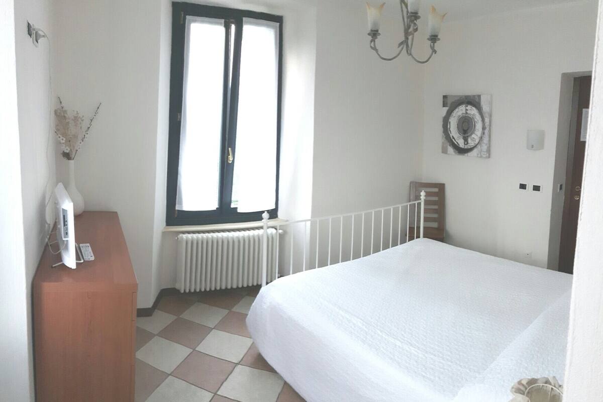 Et soveværelse med seng, radiator, et vindue og en lampe på væggen.