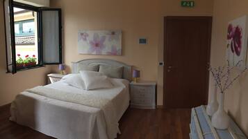 A bedroom with a bed, nightstands, a window with a view, a door, and a wall with a floral painting.