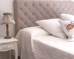 Una cama bien hecha con un cabecero capitonado, una lámpara de noche y una mesita de noche con un cajón.