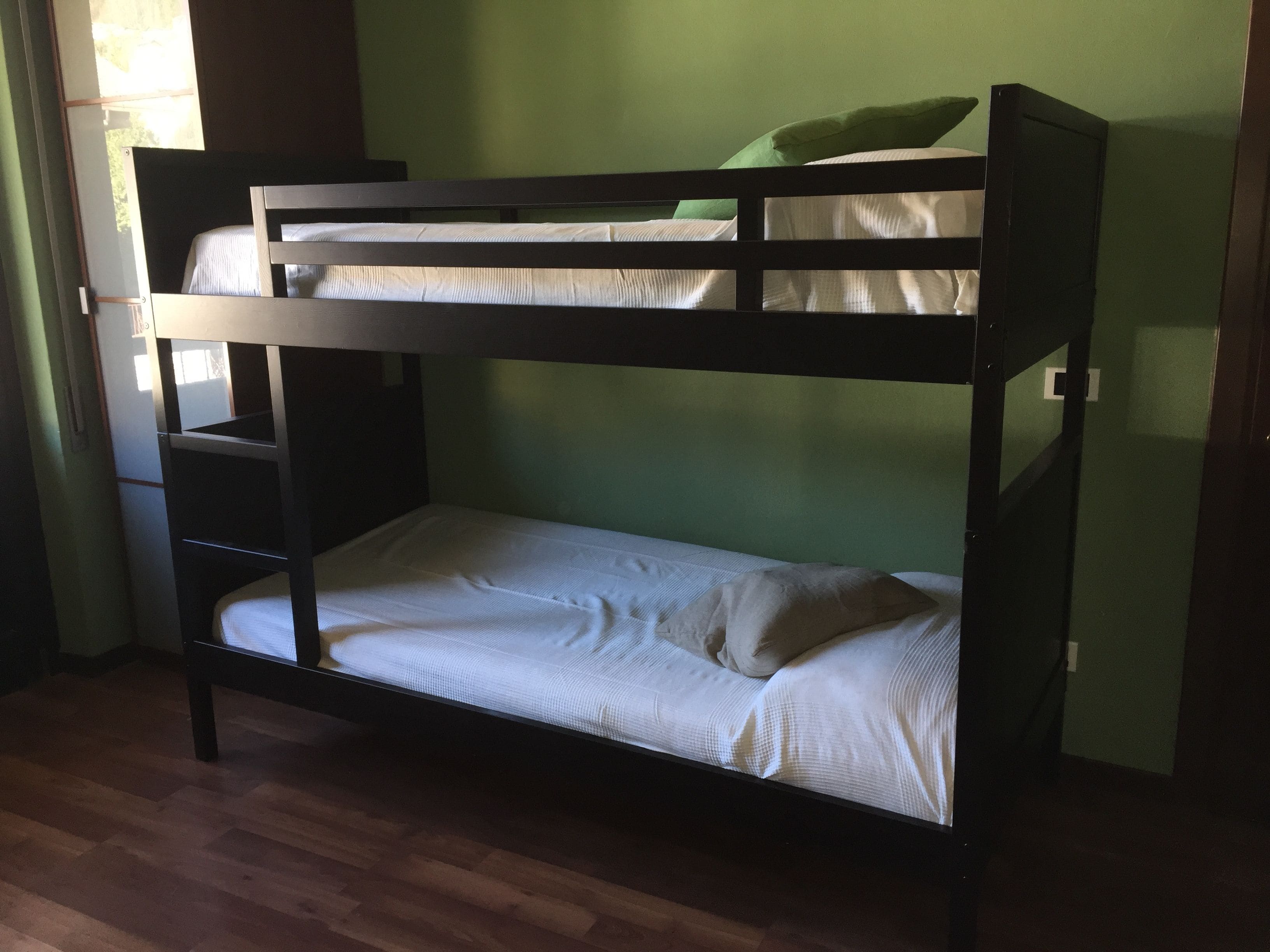 A bunk bed with two levels, a wooden frame, and white bedding.