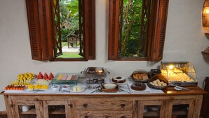 A buffet setup with various food items and a view of greenery through open windows.