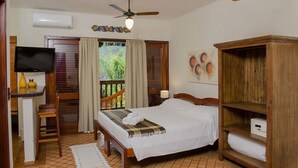 A bedroom with a bed, a wooden wardrobe, a TV, a desk with a chair, and a balcony with curtains.