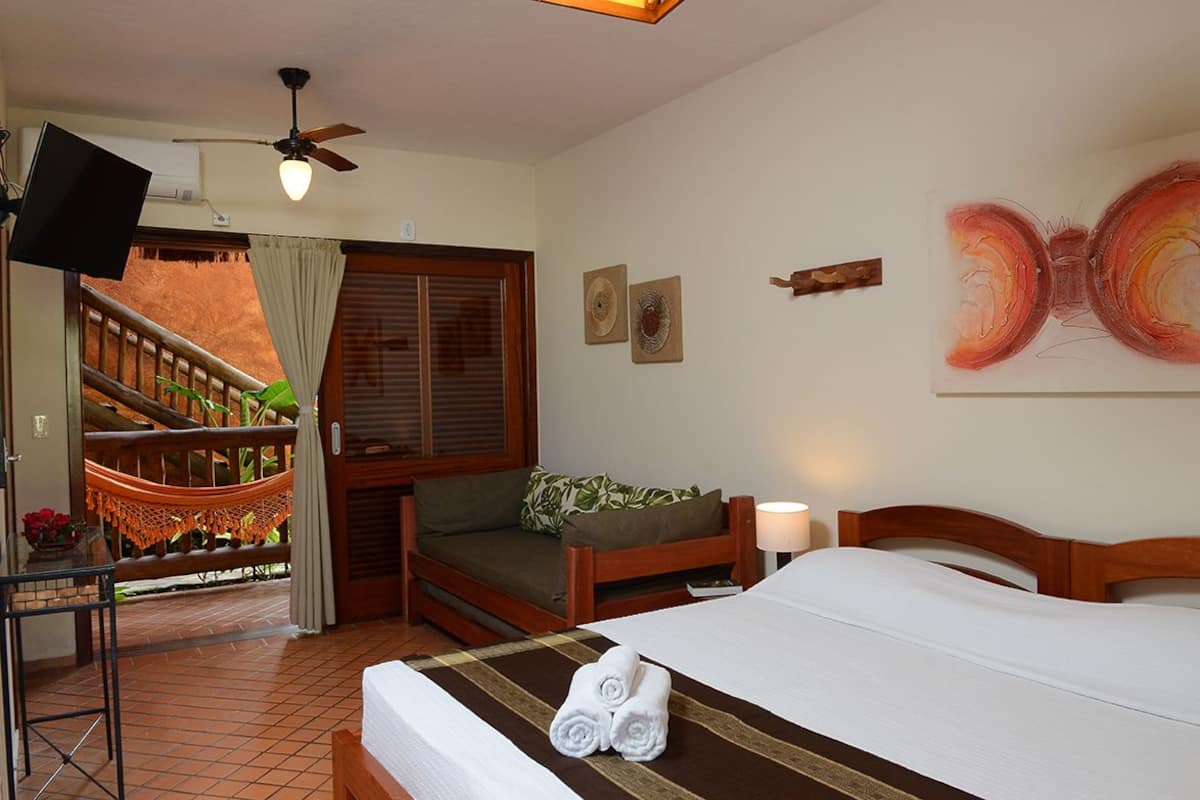 A hotel room with a bed, a desk, a chair, a balcony with a hammock, and a ceiling fan.