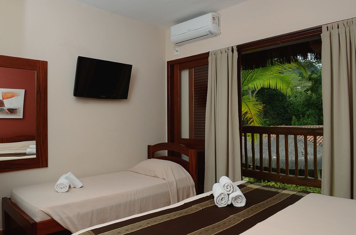Une chambre d’hôtel avec deux lits, une télévision, la climatisation et une vue sur un jardin tropical.