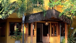 A building with a thatched roof entrance, large windows, and a potted plant in front. - Pousada Moryba (São Sebastião)