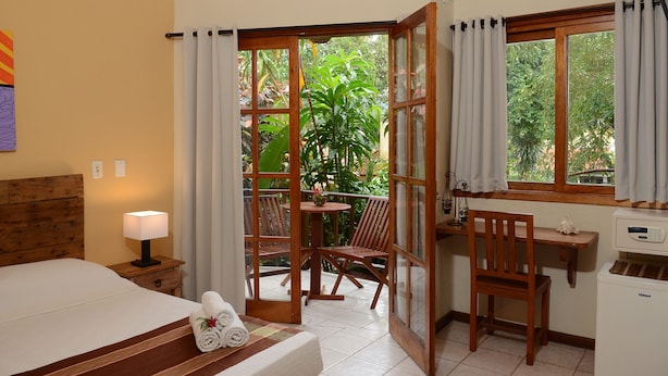 A hotel room with a bed, a desk, a chair, a table, and a window with curtains. - Pousada Moryba (São Sebastião)