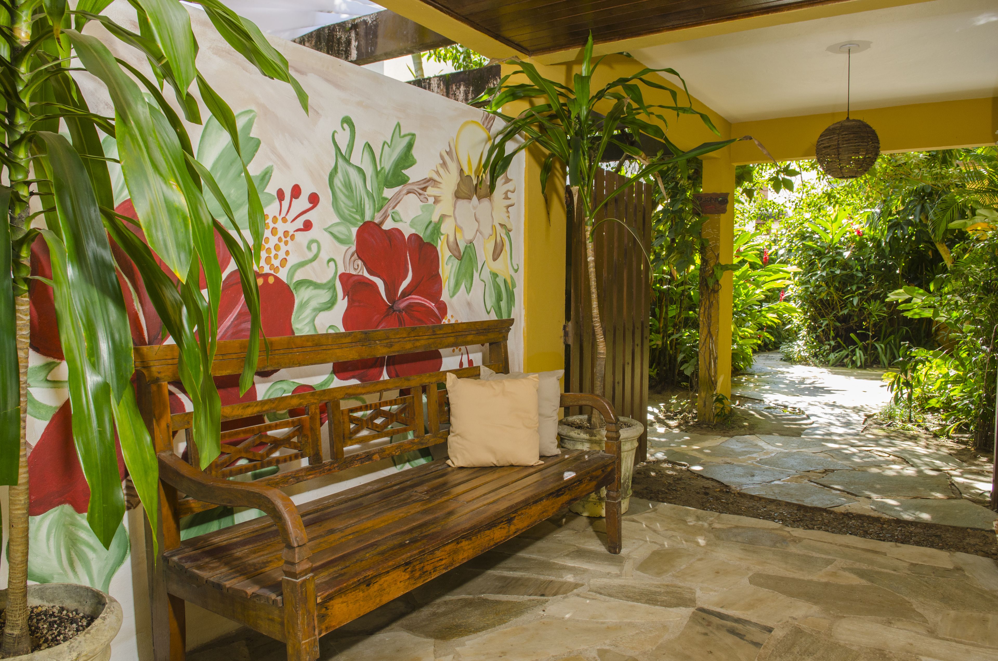 A wooden bench with cushions, a stone pathway, and a mural of flowers on a wall.