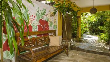 A wooden bench with cushions, a stone pathway, and a mural of flowers on a wall.