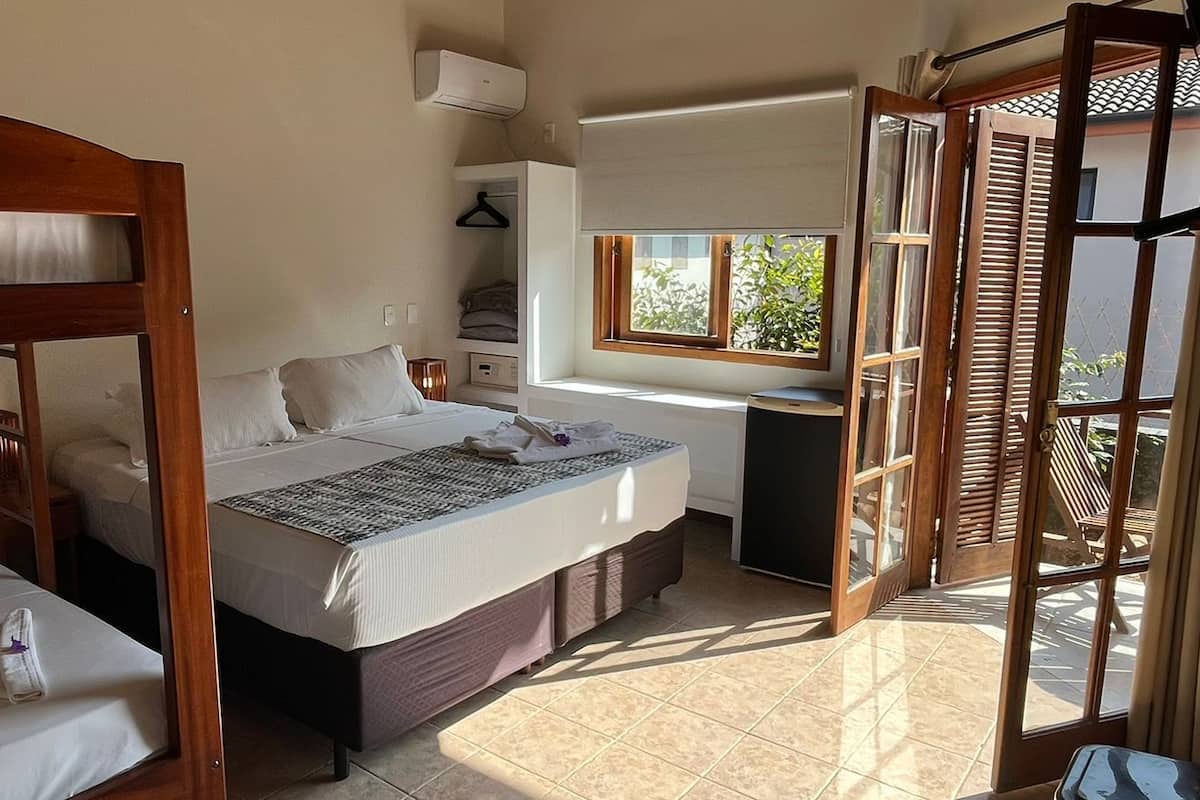 Habitación de hotel con literas, una cama individual, un escritorio con silla, una ventana y una puerta corredera a un balcón.