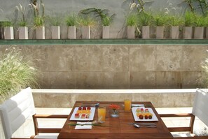 An outdoor dining table with plates of fruit and juice, set against a backdrop of tall plants and a concrete wall. - Dazzler by Wyndham Buenos Aires Palermo (Buenos Aires)