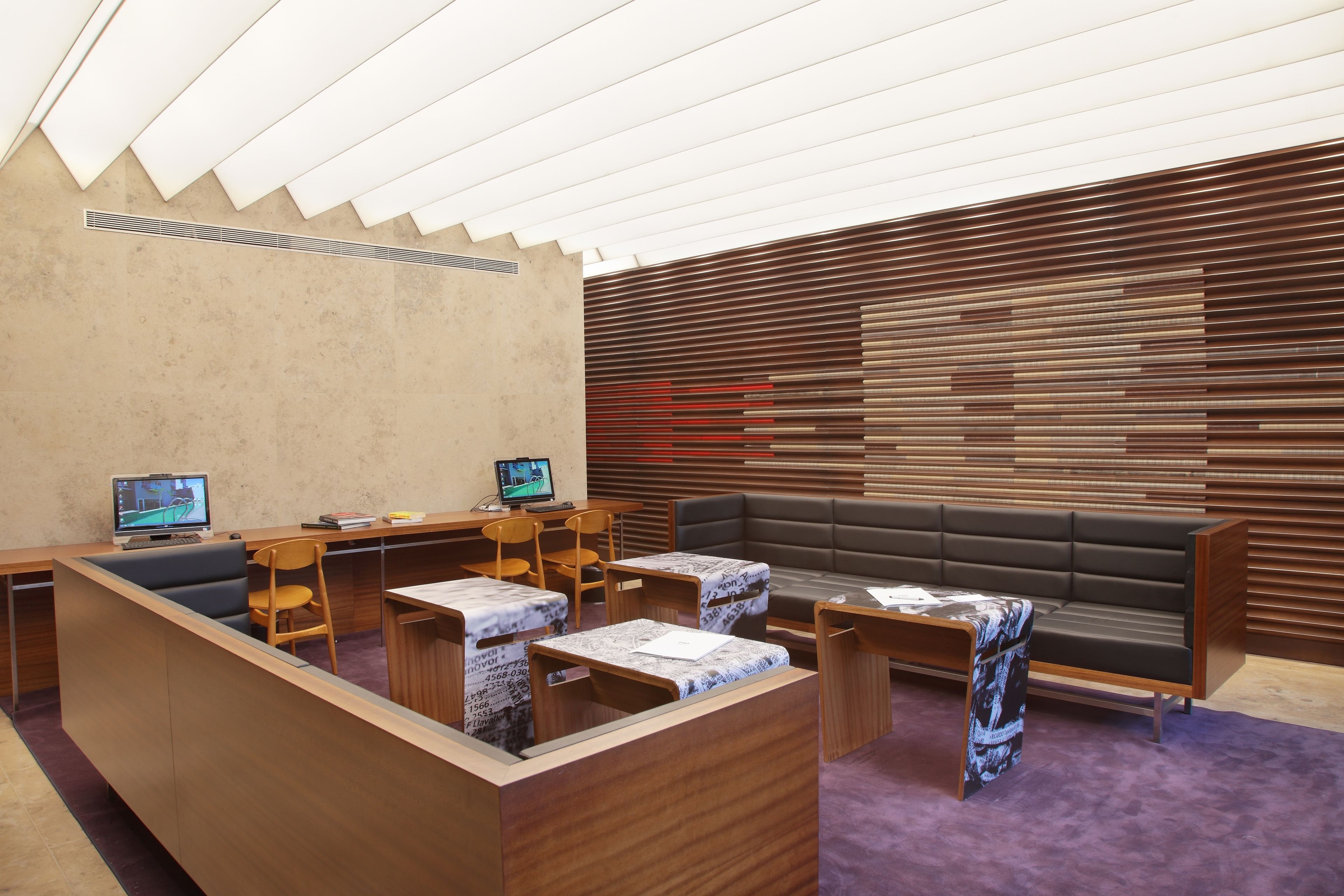 Un área de espera moderna con muebles de madera, un sofá y dos monitores de computadora.