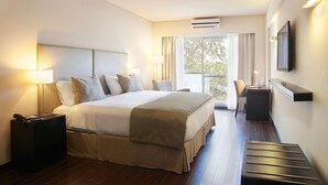 Habitación de hotel con una cama grande, mesitas de noche, un escritorio, una silla y un televisor en la pared.