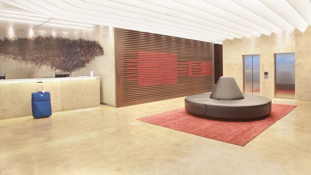 A modern reception area with a reception desk, a large abstract art piece, a seating area, and an elevator.