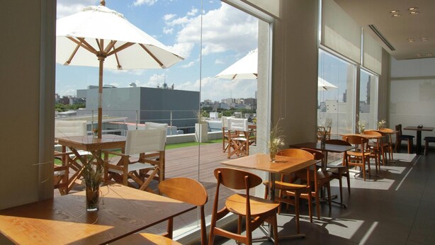 Un restaurante moderno con ventanas amplias, mesas de madera y sombrillas blancas.