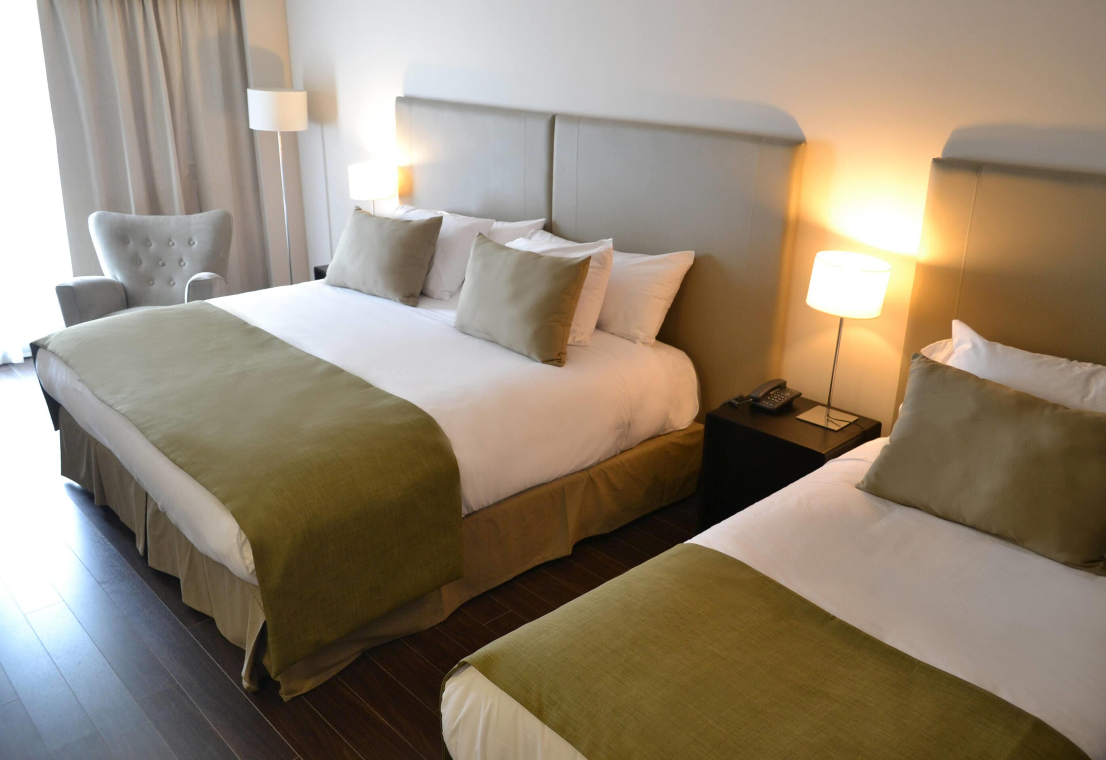 A hotel room with two beds, a chair, a lamp, and a nightstand.