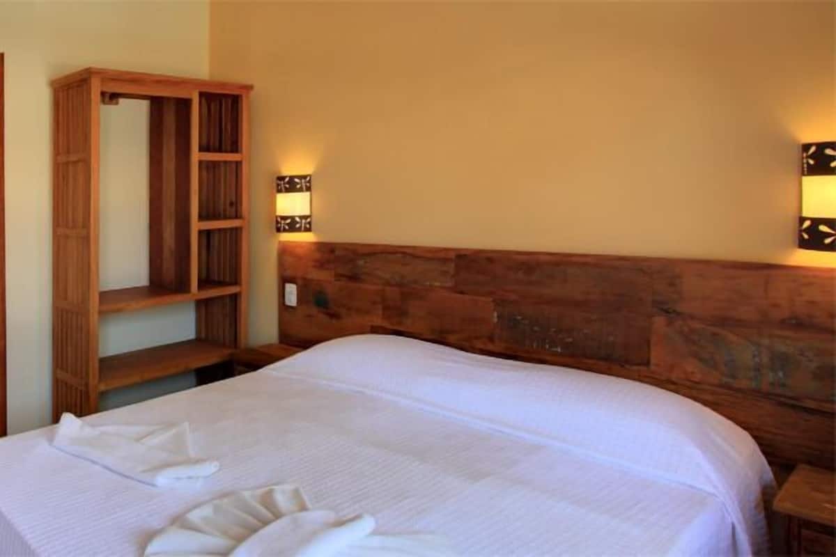 A hotel room with a bed, a bathroom with a sink and mirror, and a wooden headboard.