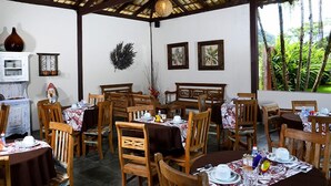A dining area with wooden tables and chairs, a white fireplace, and framed pictures on the wall. - Pousada Tupinambá (São Sebastião)