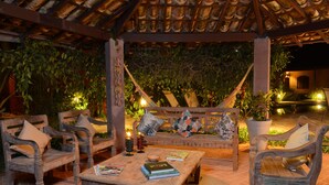 An outdoor seating area with wooden furniture and a table, surrounded by potted plants and a tiled ceiling. - Pousada Tupinambá (São Sebastião)