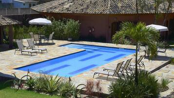A swimming pool with lounge chairs and umbrellas, surrounded by plants and a tiled roof structure.