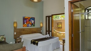 A bedroom with a wooden headboard, a bed with white linens, a colorful abstract painting, a small bedside table with a lamp, and a view of a balcony with a railing. - Pousada Tupinambá (São Sebastião)