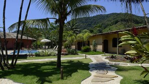 A tropical garden with a stone pathway, palm trees, and a pool area. - Pousada Tupinambá (São Sebastião)