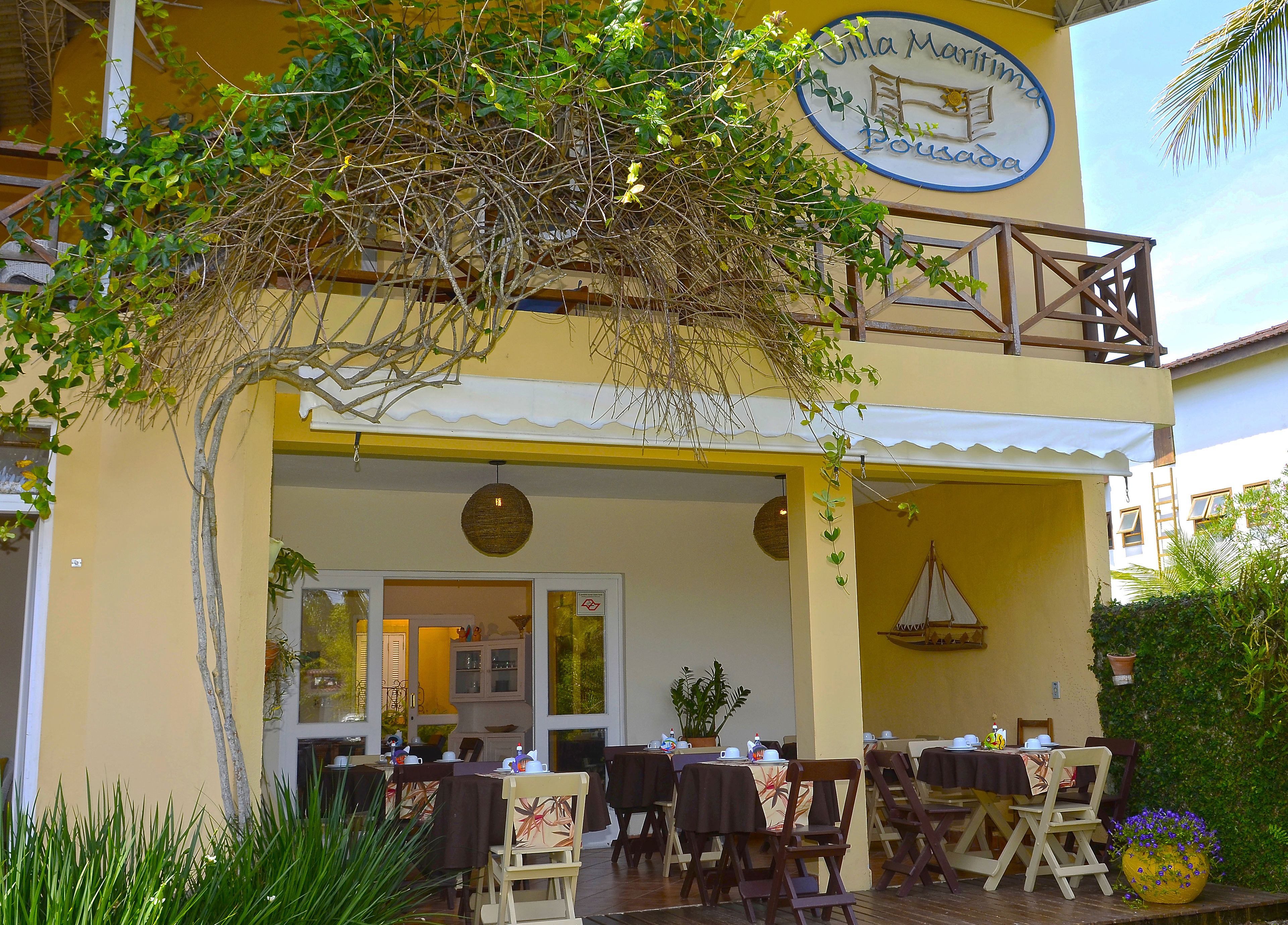 Um restaurante com mesas ao ar livre, fachada amarela e placa com o texto 'Villa Maritimus'.
