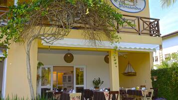 Um restaurante com mesas ao ar livre, fachada amarela e placa com o texto 'Villa Maritimus'.