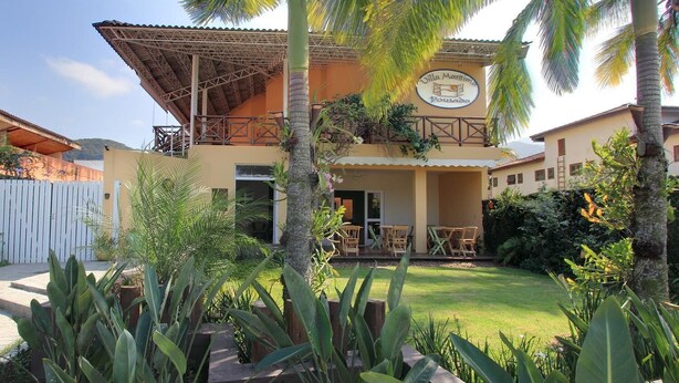 Un edifici de dues plantes amb un balcó, envoltat de vegetació tropical.