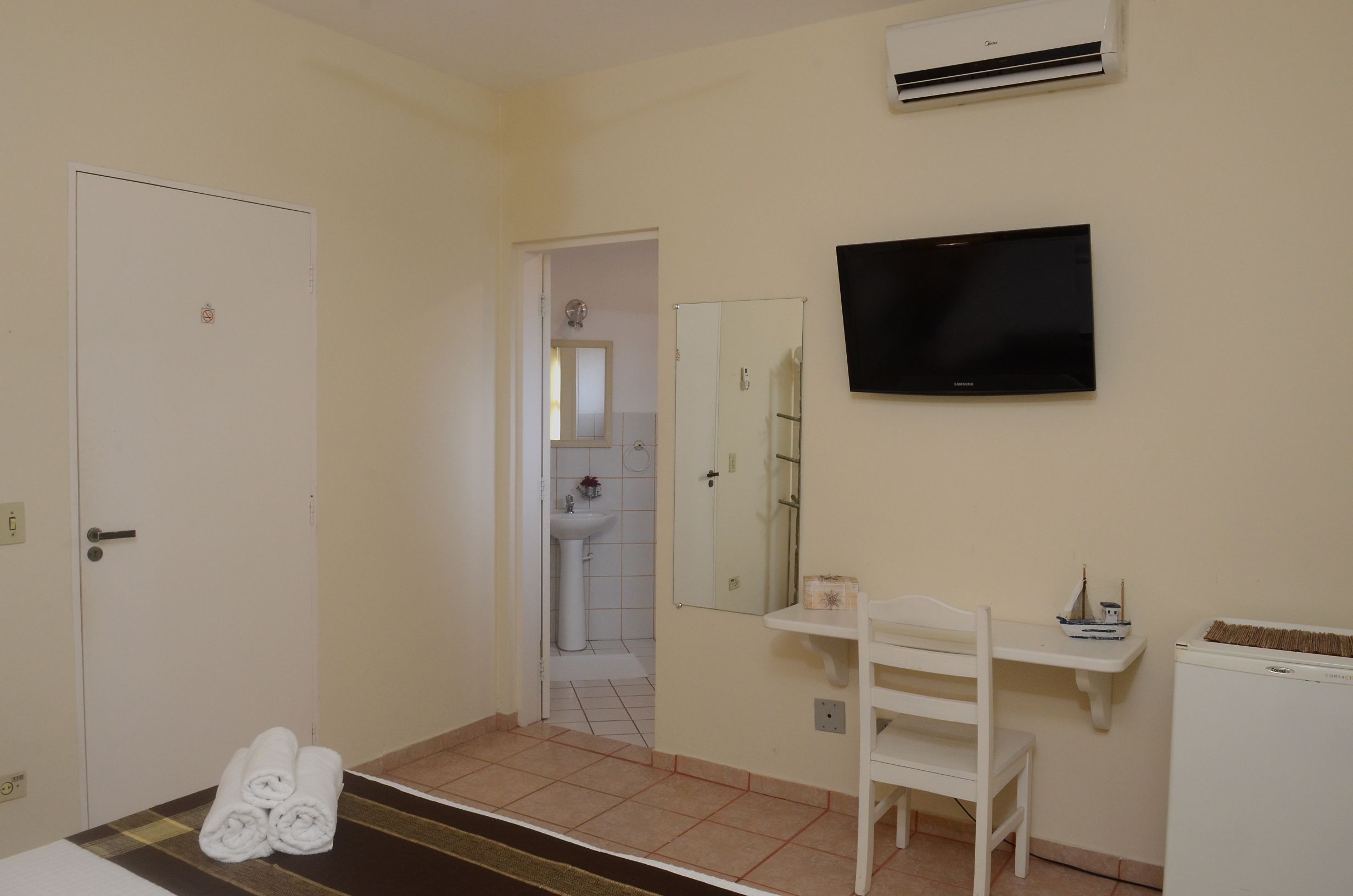 Une chambre d’hôtel comprenant un lit, un téléviseur fixé au mur, une petite table avec une chaise et une porte donnant sur une salle de bain.