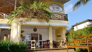 Edifici de dues plantes amb un cartell que diu "Villa Maritim Punta Bousada". Hi ha taules i cadires a l'exterior, una boscadeta de fusta i una cistella penjant.