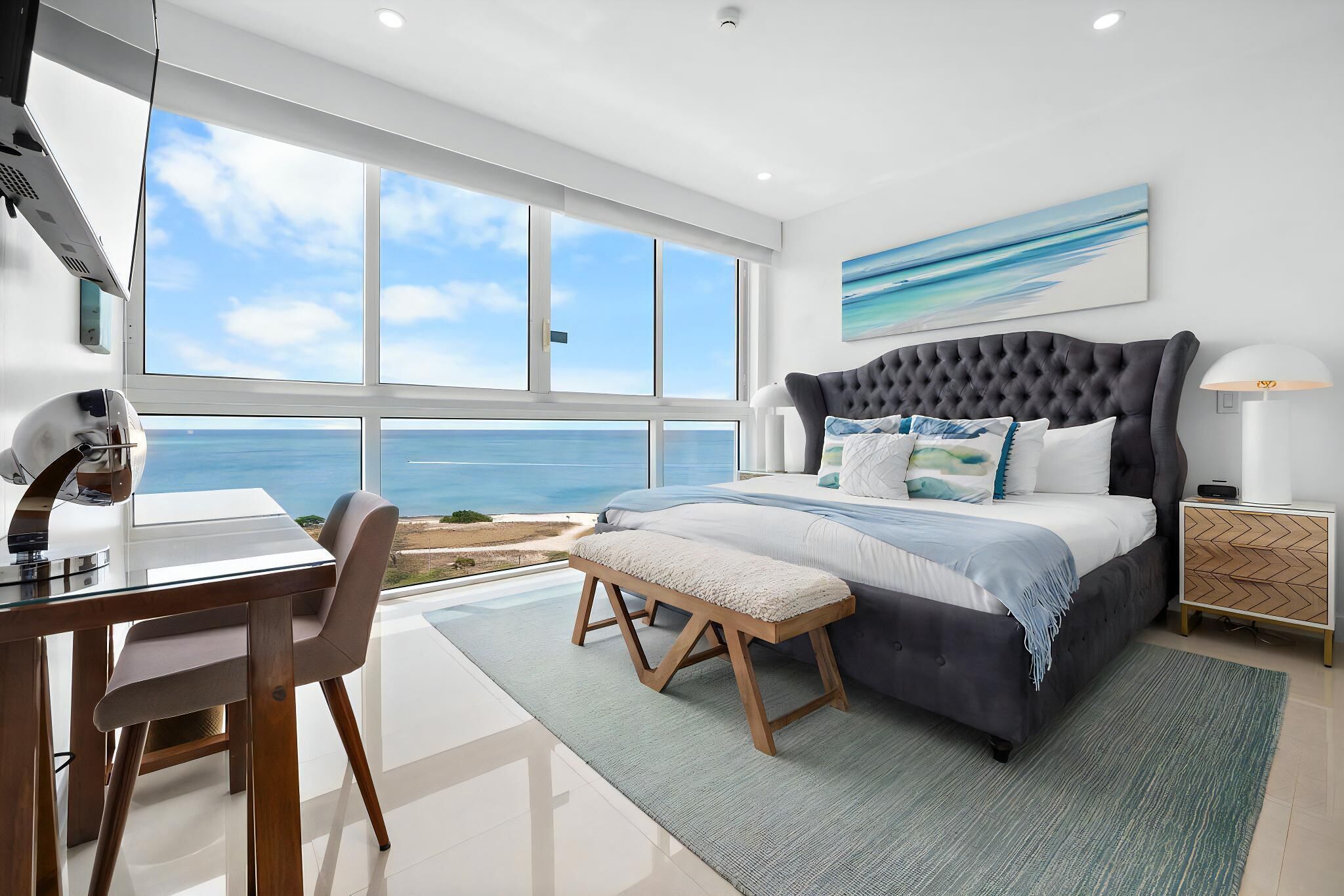 A modern bedroom with a large bed, a desk, and a view of the ocean.