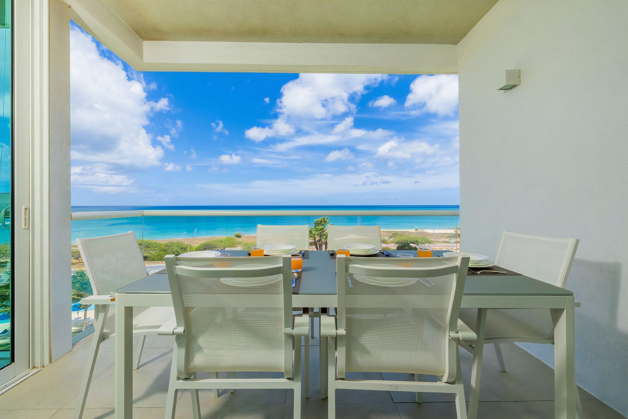 A dining area with a table and chairs, a view of the ocean, and a clear sky.