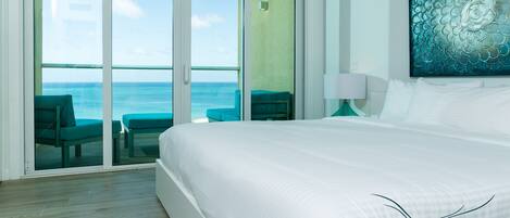 A hotel room with a large bed, a view of the ocean through a sliding door, and a painting on the wall.