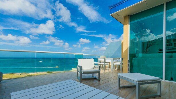 A modern outdoor deck with a view of the ocean, featuring white lounge chairs and a glass wall.