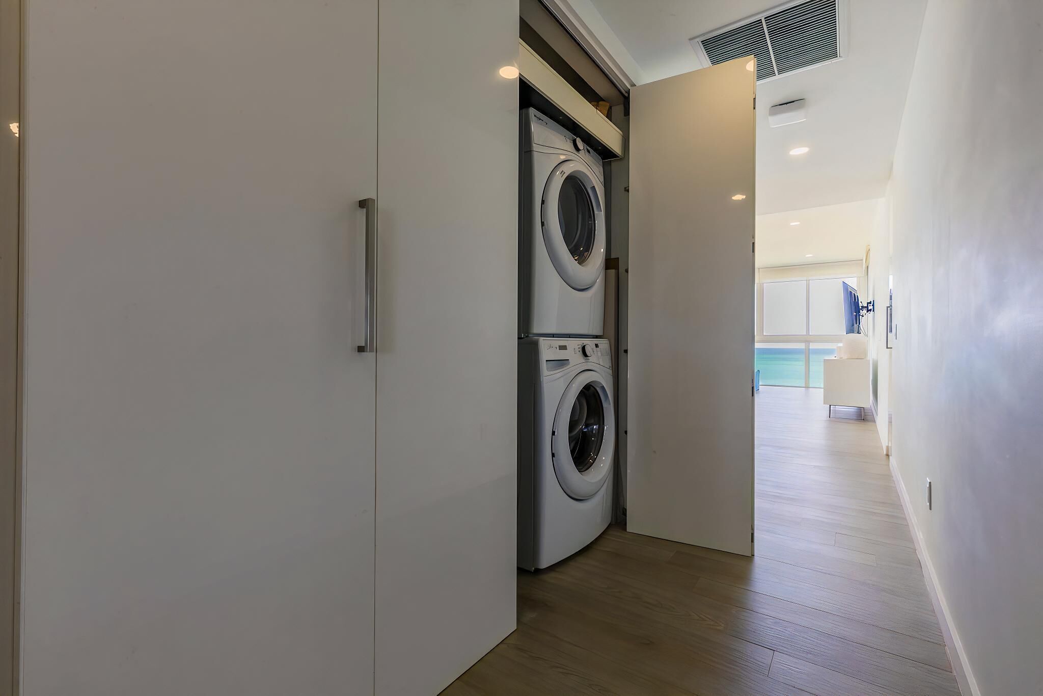 A laundry room with two stacked front-loading washing machines and a door leading to a hallway.
