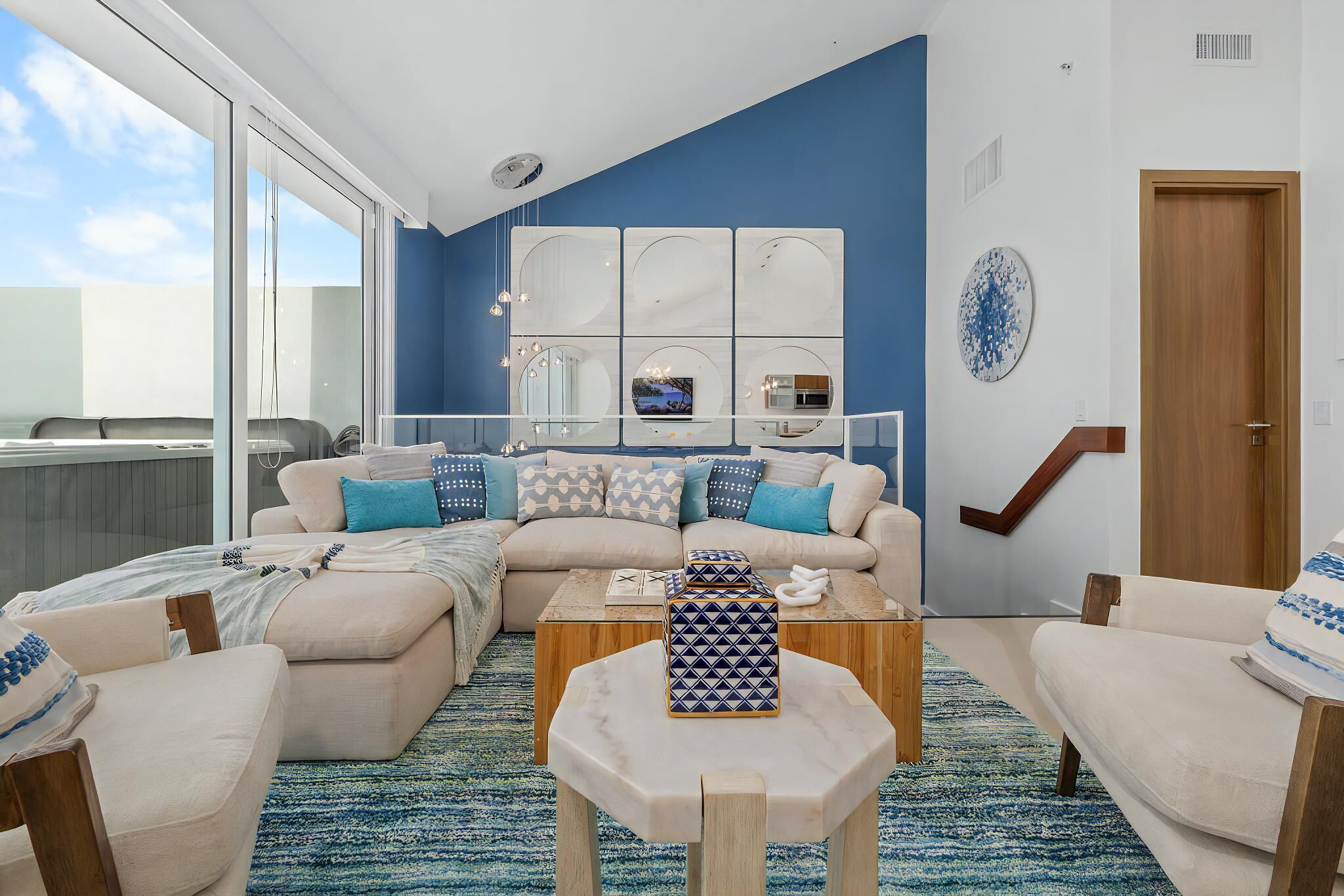 A modern living room with a large window, a sofa set, a coffee table, and a decorative mirror wall.