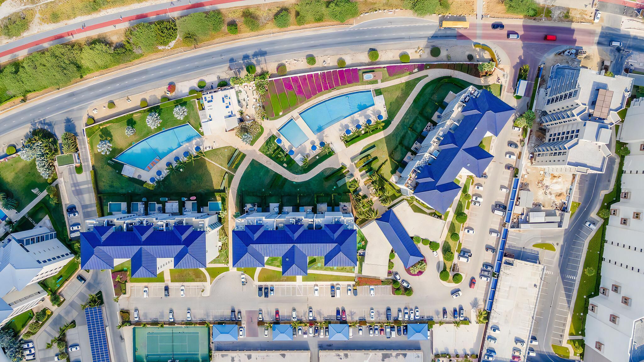 An aerial view of a hotel with multiple swimming pools, a tennis court, and a parking lot.