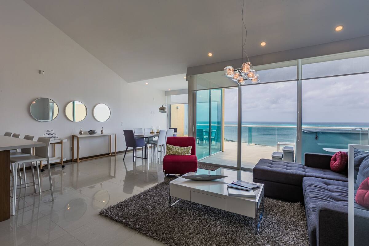 A modern living room with a large glass door leading to a balcony with a view of the sea.