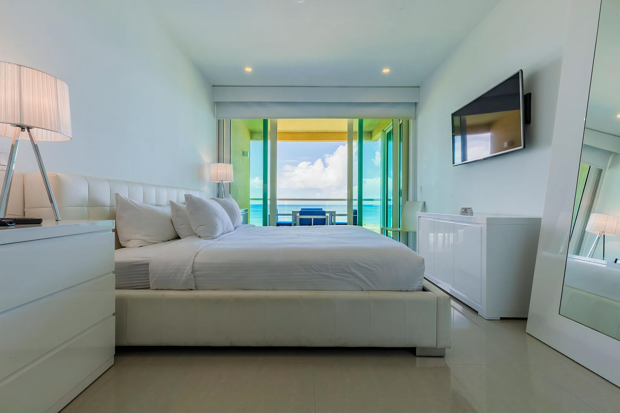 Una moderna camera d'albergo con un letto grande, una TV fissata alla parete e vista sul mare attraverso ampie finestre.