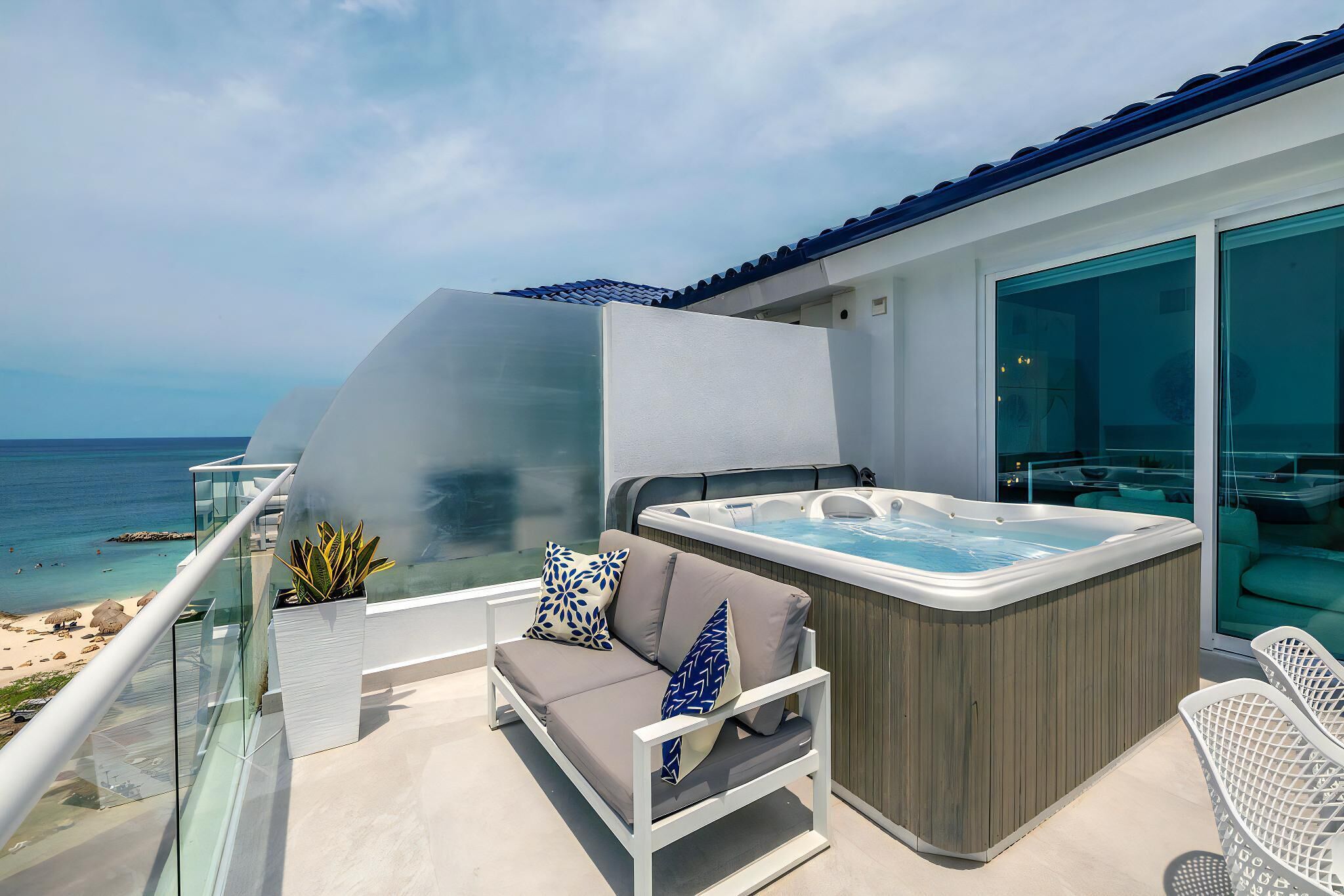 Un balcón con barandilla de vidrio, un sofá con cojines, un jacuzzi y vistas al océano.